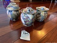 Three glazed pottery bowls with lids arranged on wooden floor, showing their hand-crafted artistic glaze with ventilation holes for garlic or potpourri use.