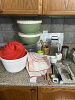 Overview of baking lot on countertop including silicone molds, mixing bowls, measuring mats, grater, pie dish, cake container, pestle and mortar, and other utensils