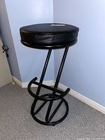 Side view of black metal frame bar stool showing round cushioned seat and circular footrest.
