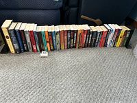 Wide view of approx. 30 assorted novels lined up on carpet with metal bookends on either side.