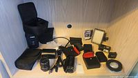 Photo showing assorted camera accessories including a Canon VIXIA HF R500 camcorder, multiple battery chargers, flashes, and lenses.