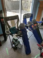 Photo showing 6 oversized mesh folding chairs by Ozark Trail with cup holders, their canvas carrying bags, 2 grill baskets, lunch bag and umbrella arranged in a room.