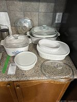 Full view of 6 vintage CorningWare dishes with lids showing vintage blue cornflower pattern, white ribbed designs and various glass and plastic lids.
