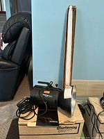 Studio flash head with power cord placed atop the original Courtenay Lighting Corp box alongside the large folded white photo umbrella.