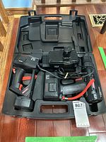 Set components including drill, flashlight, charger, batteries arranged in molded hard plastic case on wooden floor.