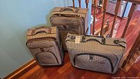Large suitcase, carry-on, and garment case in matching houndstooth fabric with brown trim on hardwood floor by wall