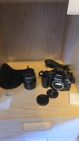 Photo showing Nikon F90X camera body with strap, Tamron 90mm lens with front lens cap attached, additional lens cap on the surface, and black cloth storage bag.