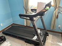 Full side view of NordicTrack treadmill showing running belt, handrails, and console with manual placed on top.