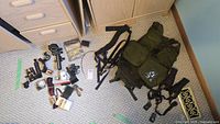 Wide shot showing all lot items arranged on carpet, including harness vest, Nikon bellows, cords, filters, and accessories