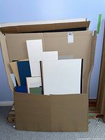 Cardboard box containing various photography mattes of different sizes and colors including white, black, blue, tan, and green.