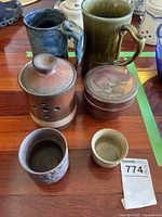 Six pottery items displayed on wooden floor including two large Irish Wade mugs, two garlic bowls with lids, and two small cups