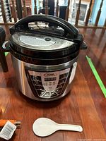 Photo showing the pressure cooker from a top angle with lid and white plastic spoon beside it
