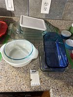 Photo of various Pyrex rectangular and round glass casserole dishes on countertop along with one white rectangular plastic Tupperware lid