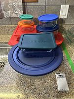 Various rectangular and round Pyrex glass containers stacked with colorful plastic lids on a kitchen counter.