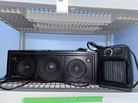 Hitachi black portable radio with cassette player and portable ceramic space heater on a plastic shelf.