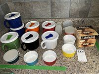 View of all soup mugs with silicone lids, ramekins with lids, and boxed ceramic garlic dish on kitchen counter