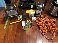 Overview of the lot items on a wooden floor including portable work light, extension cords, door knob, hand tools, adhesive, and timer