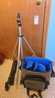 Adjustable aluminum tripod with three legs and mounting head, a black belt, and the Lowepro camera bag placed on the floor.