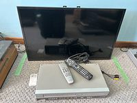 Samsung 32-inch TV, Philips VHS/DVD combo player, and two remote controls shown together on the carpeted floor.