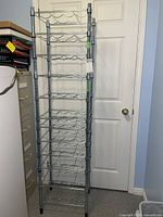 Full height view of chrome metal wine rack standing next to door, showing multiple tiers for bottle storage