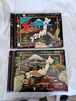 Two lacquered wooden photo albums, front view showing painted detailed Japanese maps, Mount Fuji, temples, birds, and bridges