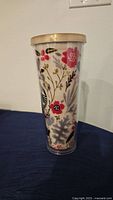 Full side view of the clear plastic Starbucks tumbler with colorful floral pattern and beige lid, standing on a dark surface against a white wall.