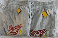 Close-up of two pairs of gray sweatpants laid out showing the 'Racing Club' embroidered logo with lightning bolt and original tags