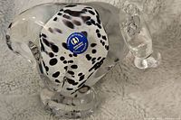 Side and top view showing the clear glass cow paperweight with black and white speckles and a blue sticker on its base.