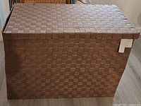 Front view of the rectangular caramel-colored cloth storage bin with lid and tag visible on the corner