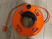Top view of bright orange heavy duty extension cord wound on a portable scrolling reel with multiple slots and a handle.