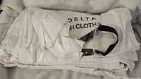 Stack of folded white cloth wash cloth bags with black handles, Delta branding visible under plastic packaging
