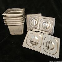 Stack of six aluminum warmer inserts with five lids placed on a black backdrop.