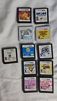 Photo showing 11 assorted Nintendo DS and Nintendo 3DS game cartridges arranged on white fabric. Titles and labels clearly visible.