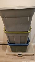 Four stacked assorted plastic storage bins in grey, olive green, blue, and translucent colors