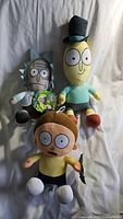 Three Rick and Morty character plush toys arranged on a fabric surface.