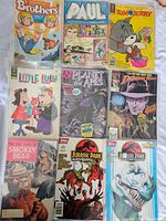 Top view of 9 vintage comic books including Adventure Brothers, Paul, Tom & Jerry, Little Lulu, Planet of the Apes, Indiana Jones, Smokey Bear, Jurassic Park Adventures.