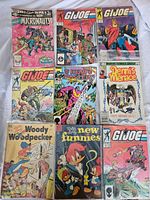Photo showing 9 vintage comic books: Micronauts, several GI Joe issues, Headmasters, Dennis the Menace, Woody Woodpecker, and New Funnies.