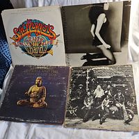 Four vinyl records shown: The Beatles Sgt. Pepper's Lonely Hearts Club Band, black and white kneeling woman cover, Buddha and the Chocolate Box, group photo cover