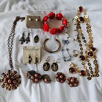 Photo shows assorted vintage and modern costume jewelry including necklaces, earrings, bracelets, rings, and brooches arranged on white fabric.
