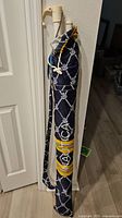 Nautica beach umbrella folded and in covering bag, showing navy blue and white rope and anchor pattern with yellow Nautica logos.