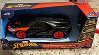 Spider-Man themed Miles Morales 2017 Ford GT radio control car in box showing front and side with black and orange paint and red wheels, USB charging feature.