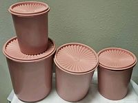 Five pink plastic Tupperware nesting containers with lids stacked and arranged from largest to smallest.