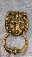 Front view of vintage brass lion head door knocker on a soft fabric background