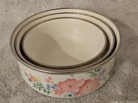 Three nesting enamel bowls stacked inside each other showing the floral design and size variation.