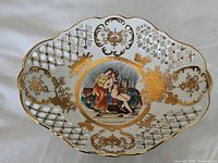 Top view of the oval porcelain footed bowl showing the central painted classical scene, lattice gold design, and scalloped edges.