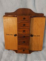 Front view of the wooden sewing tool chest with both doors closed and drawer labels visible.