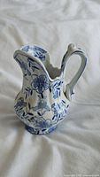 Side profile of vintage blue and white porcelain creamer showing floral patterns and scalloped spout