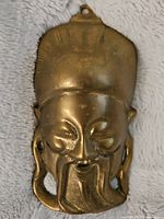 Front view of bronze wall mask showing detailed facial features and hanging loop on top.