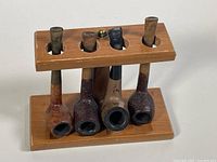 Four vintage tobacco pipes displayed vertically in wooden pipe stand on a white surface, front angle, showing pipe bowls facing forward.