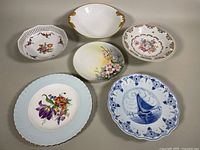 Photo of all six assorted old bone china dishes arranged in a semi circle showing various floral and scenic designs, including the Limoges footed bowl and other decorative plates.